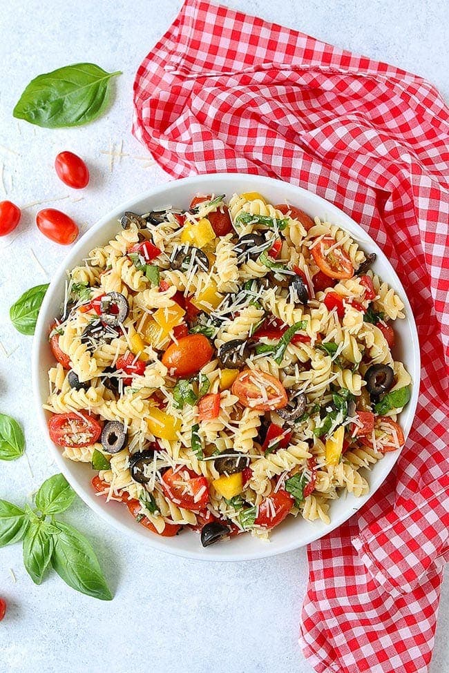 Pasta Salad with tomatoes, peppers, olives, basil, and Parmesan cheese in bowl. 