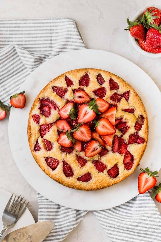 homemade strawberry cake with fresh strawberries on top on white round marble board. 