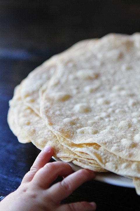 small hand reaching for plate of homemade flour tortillas 