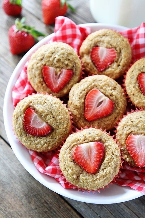 whole wheat banana muffins with strawberries on top piled in bowl