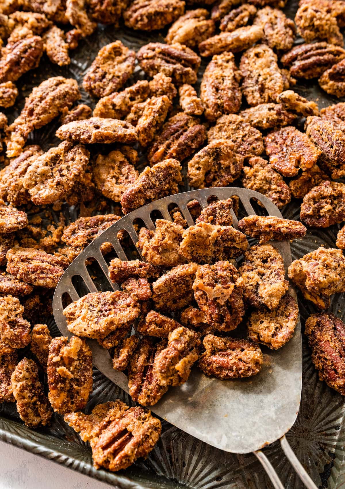 candied pecans on baking sheet with metal spatula.