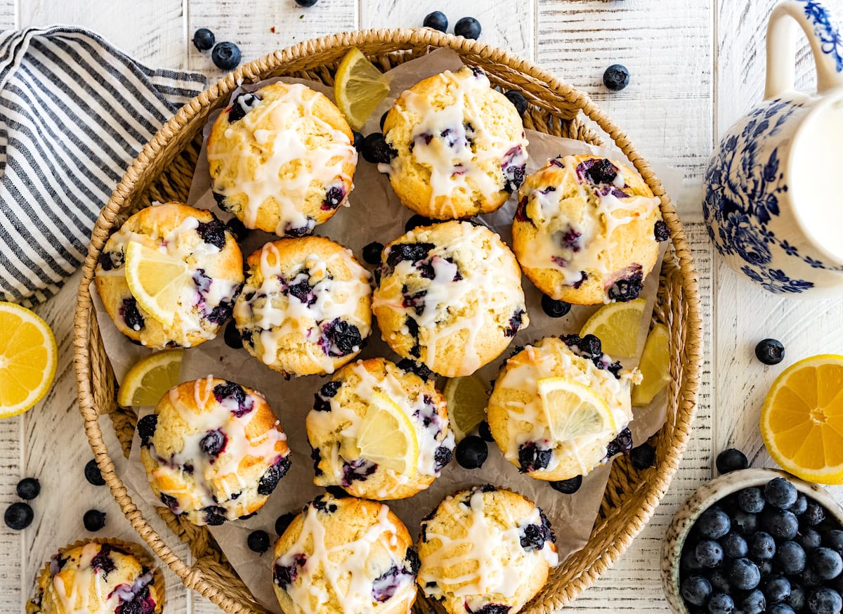 lemon blueberry muffins with lemon glaze in a basket tray with fresh blueberries. 