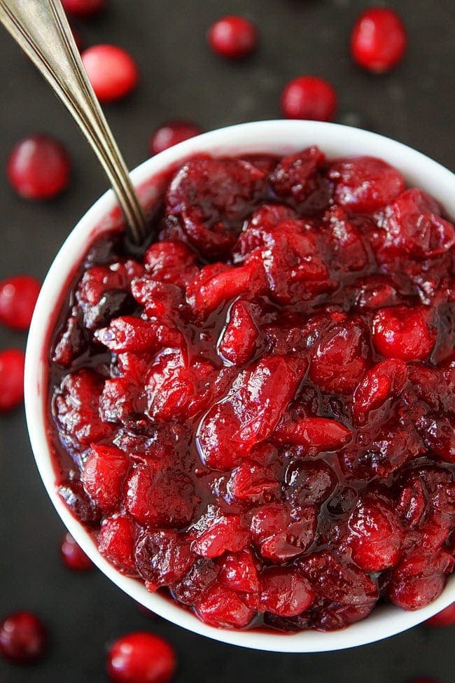 Maple Cranberry Sauce Recipe-Fresh cranberry sauce sweetened with pure maple syrup, orange zest, orange juice, and a hint of cinnamon. This is the BEST cranberry sauce recipe! Add it to your Thanksgiving and Christmas menus. fresh cranberry sauce in bowl with spoon.