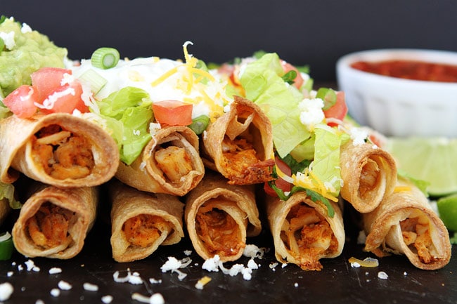 rolled chicken taquitos with toppings on pan. 