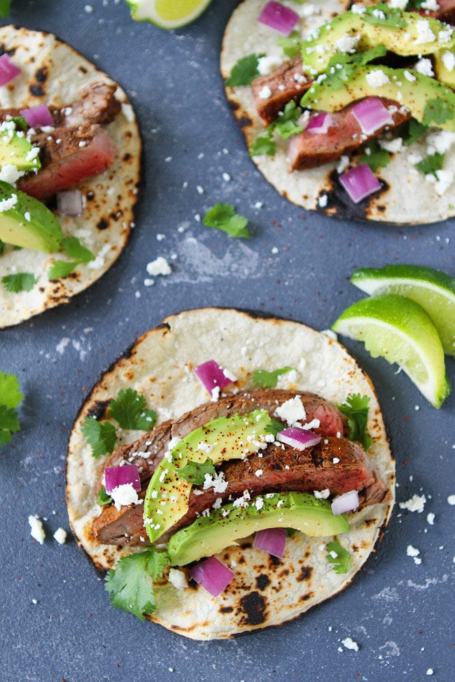 Grilled Chili Lime Steak Tacos with red onion, avocado, cilantro, queso fresco and served on corn tortillas