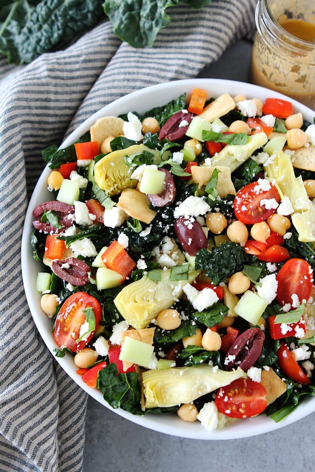 Mediterranean Kale Salad with chickpeas, tomatoes, cucumber, red pepper, artichoke hearts, olives, feta cheese, pita chips and a simple hummus dressing. This healthy salad is great as a main dish or side dish.