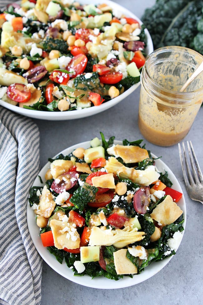 Mediterranean Kale Salad with chickpeas, tomatoes, cucumber, red pepper, artichoke hearts, olives, feta cheese, pita chips and a simple hummus dressing. This salad is perfect for lunch, dinner, potlucks, and parties!