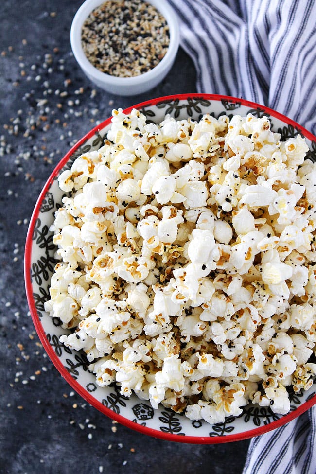 everything bagel popcorn in a bowl on a table next to a napkin and ramuken of everything bagel seasoning