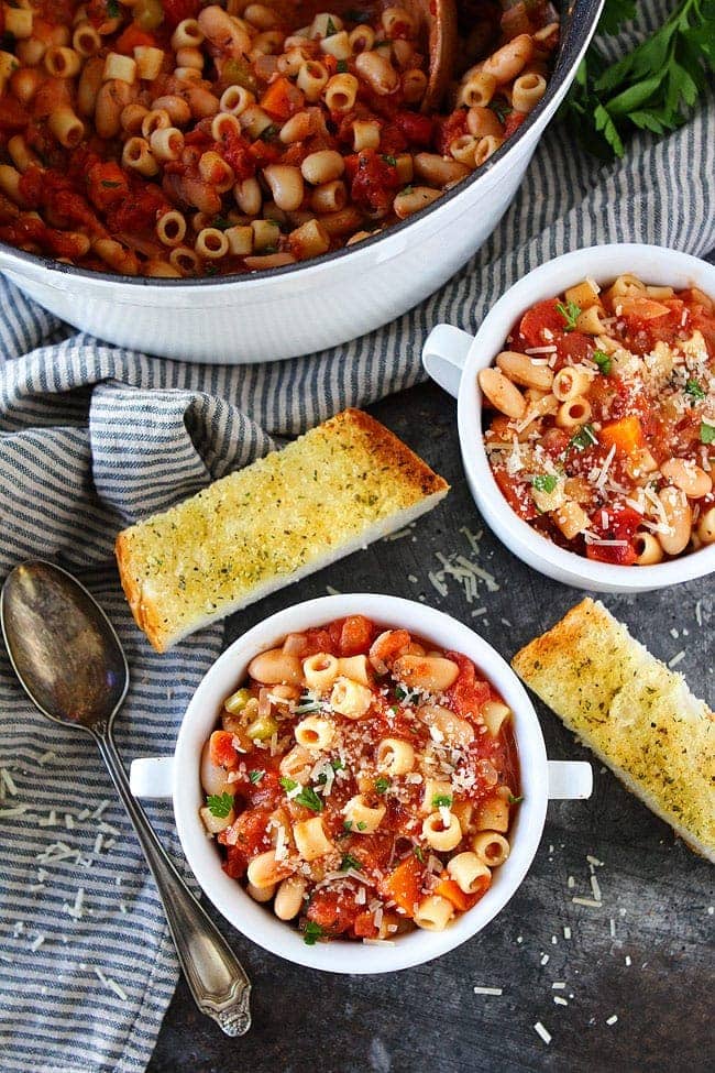 Pasta fagioli in bowls and in pot with garlic bread.