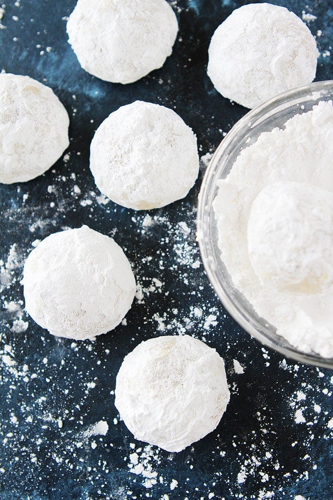 Mexican wedding cookies being rolled in powdered sugar in bowl. 