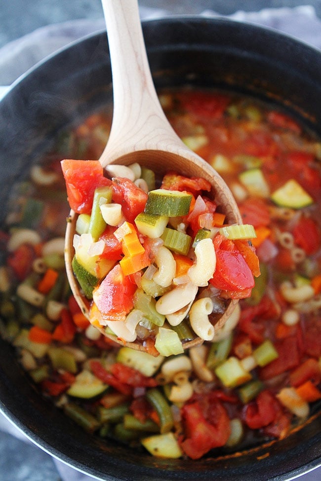 Minestrone soup in pot being served in a wooden ladle. 