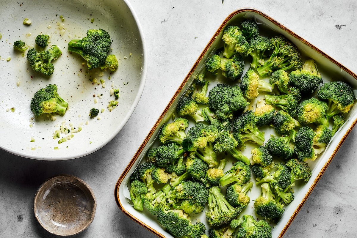 Broccoli florets transferred from a bowl into a baking pan.