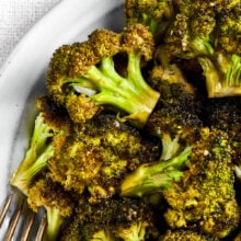 Close up of a bowl of roasted broccoli next to a fork.