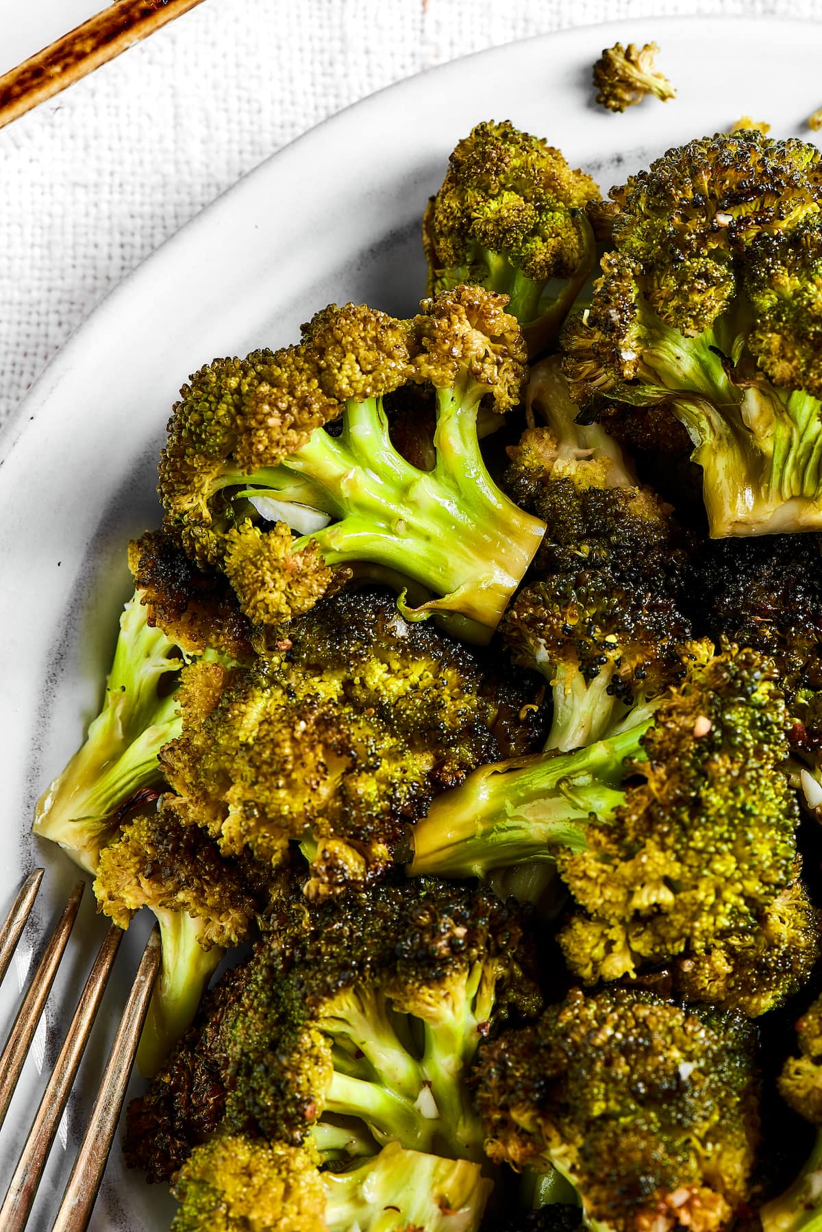 Close up of a bowl of roasted broccoli next to a fork.