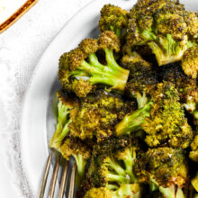 Close up of a bowl of roasted broccoli next to a fork.