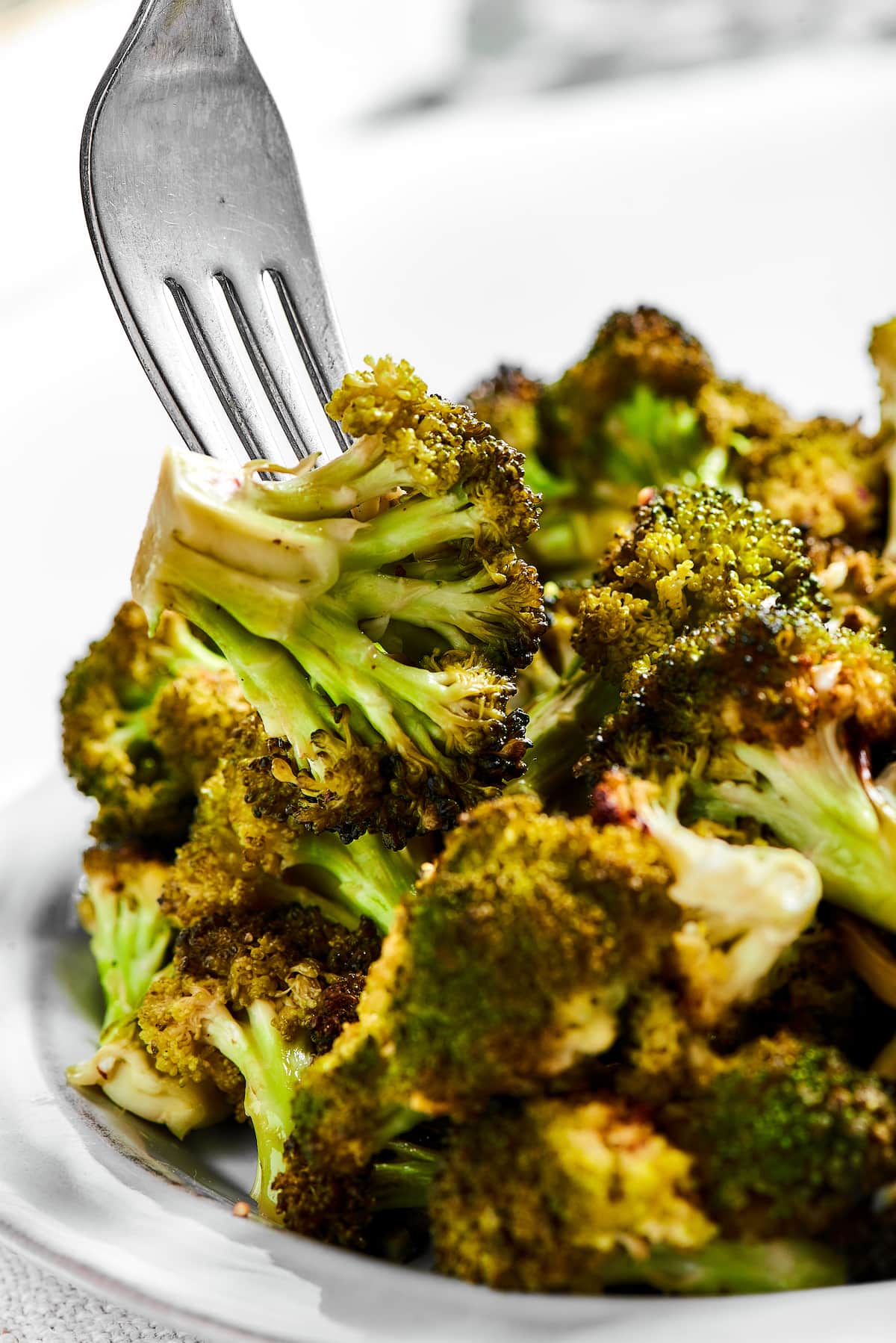 A fork picks up a broccoli floret from a bowl of roasted broccoli.