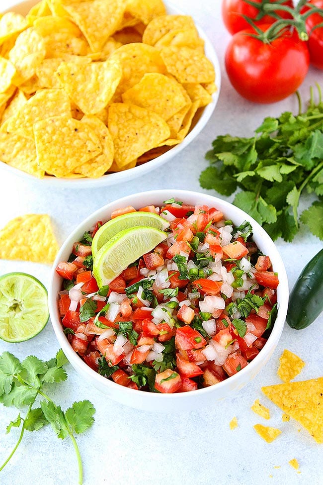 PIco de Gallo in bowl with lime wedge and tortilla chips. 