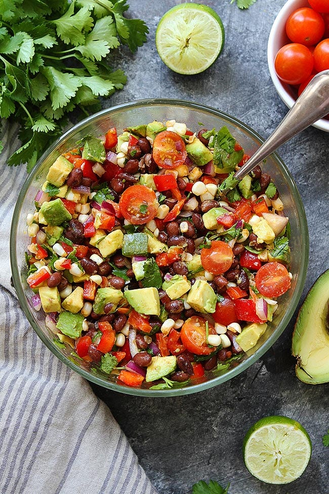 Black Bean Salad with corn, avocado, tomatoes, red pepper, cilantro, and lime. The perfect summer side dish to any meal! You can also serve it as a dip with tortilla chips! #blackbean #vegetarian #vegan #glutenfree #easyrecipe #healthyrecipe #avocado #corn #summer #saladrecipe Black Bean Salad in glass bowl with spoon.
