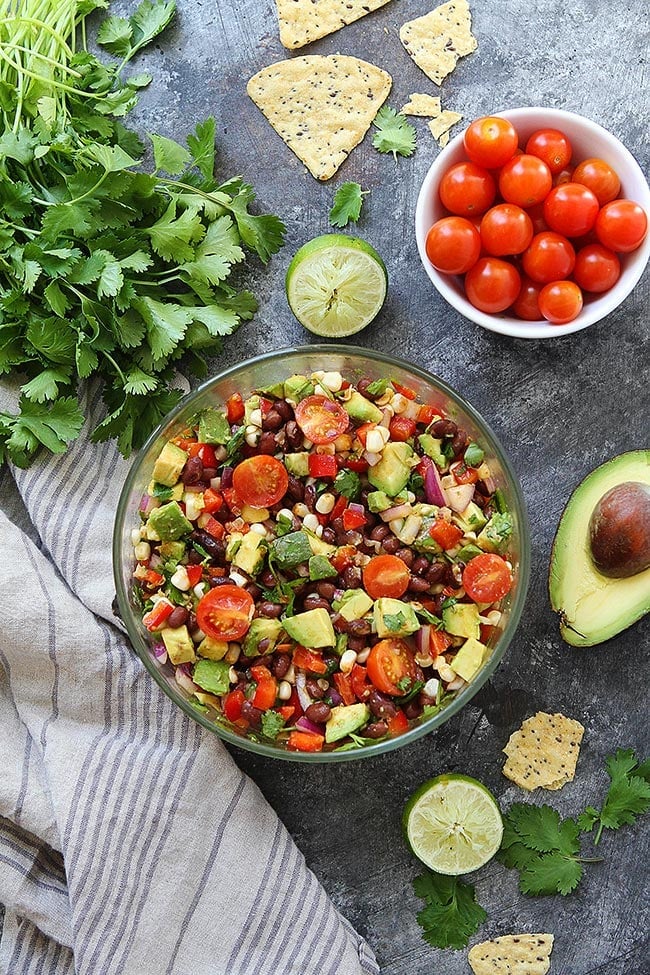 Black bean salad in bowl with cilantro, tomatoes, lime, avocado, and chips. 