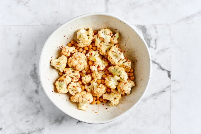 A bowl of cauliflower and chickpeas tossed with olive oil, lime juice, cumin, chili powder, onion powder, garlic powder, and salt