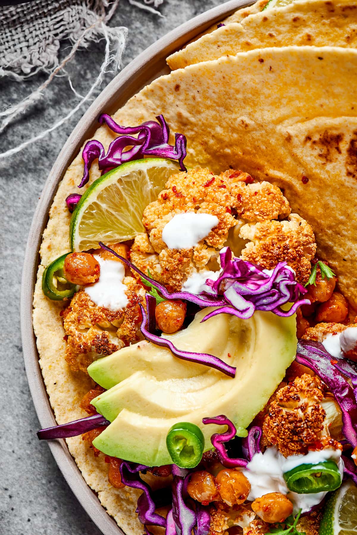 Close up of half a roasted cauliflower and chickpea taco, topped with avocado, lime crema, and fresh jalapeños