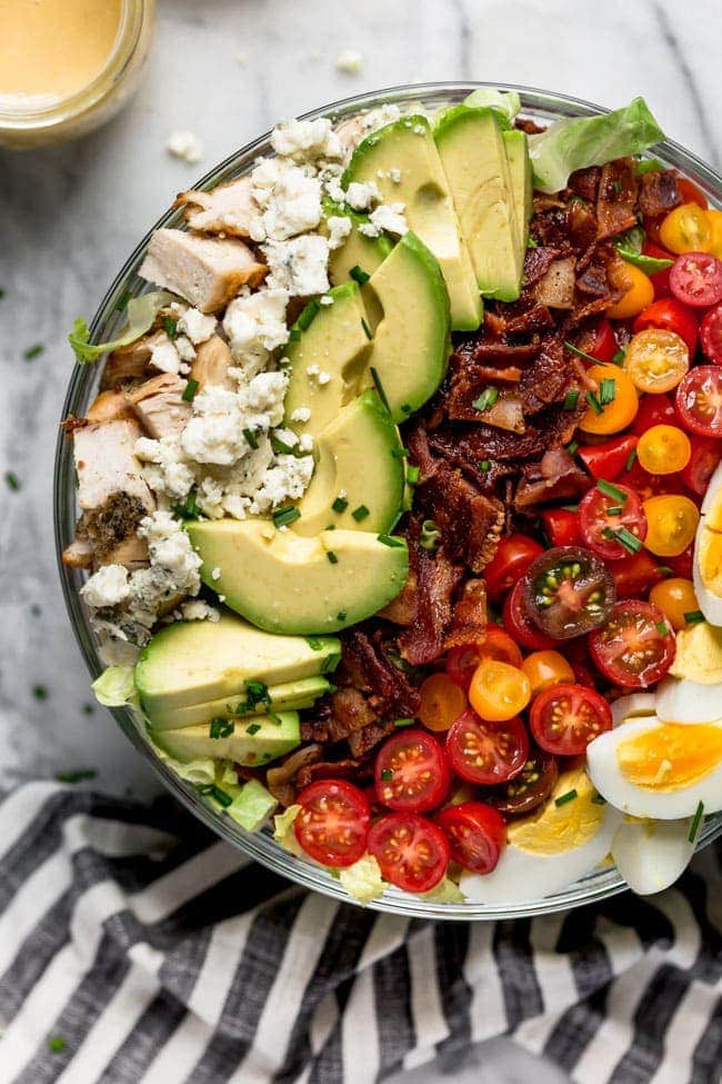 Cobb Salad with chicken, blue cheese, avocado, bacon, tomatoes, and hard boiled eggs in a large bowl.