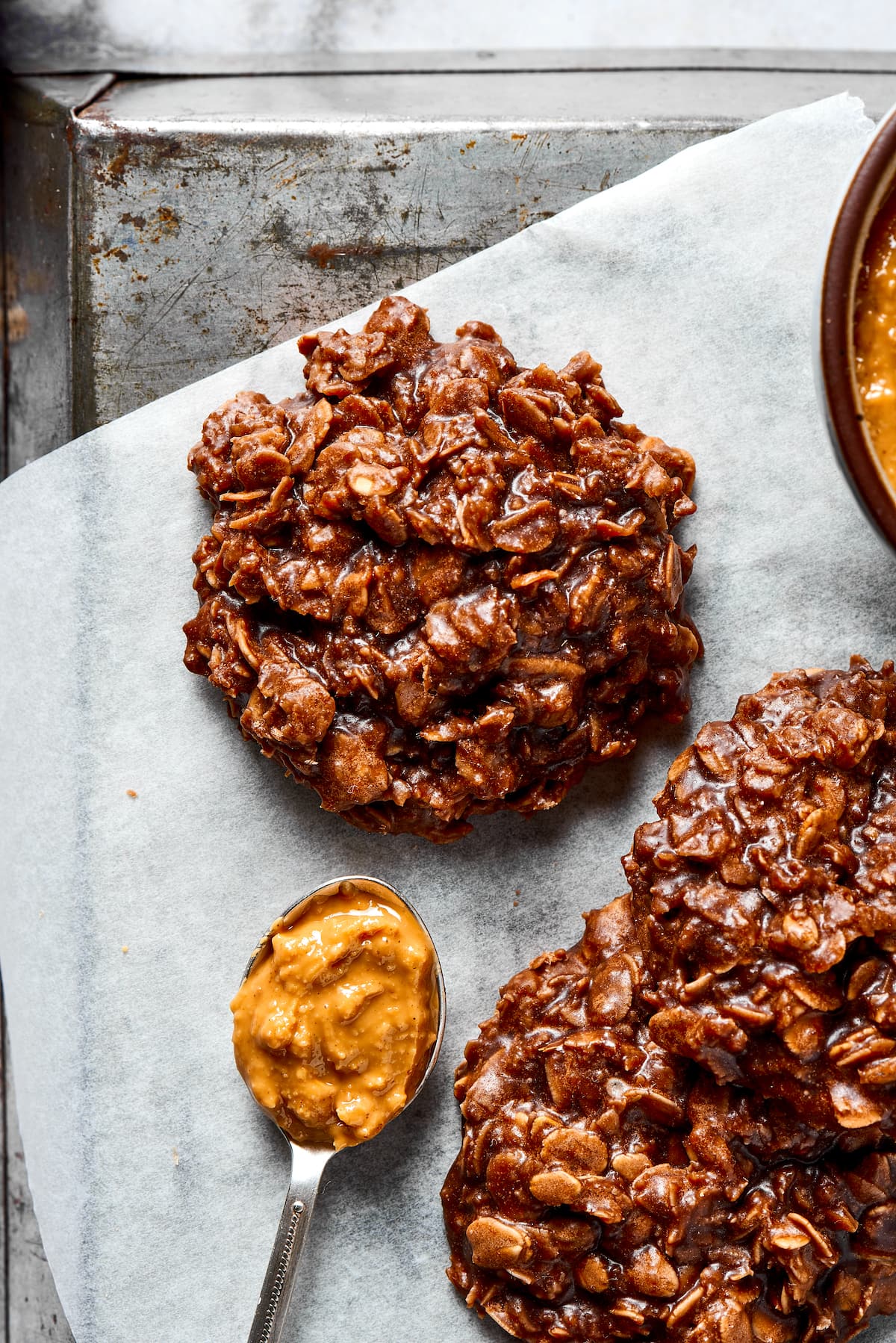 Three no bake cookies on a piece of parchment paper, next to a spoonful of peanut butter