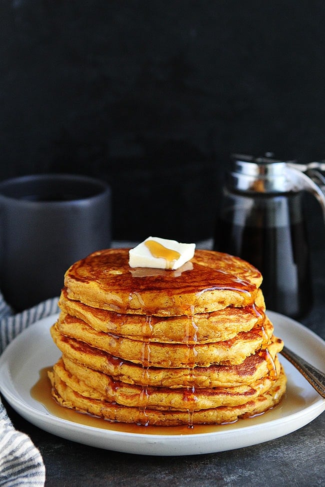 stack of pumpkin pancakes with maple syrup on plate.