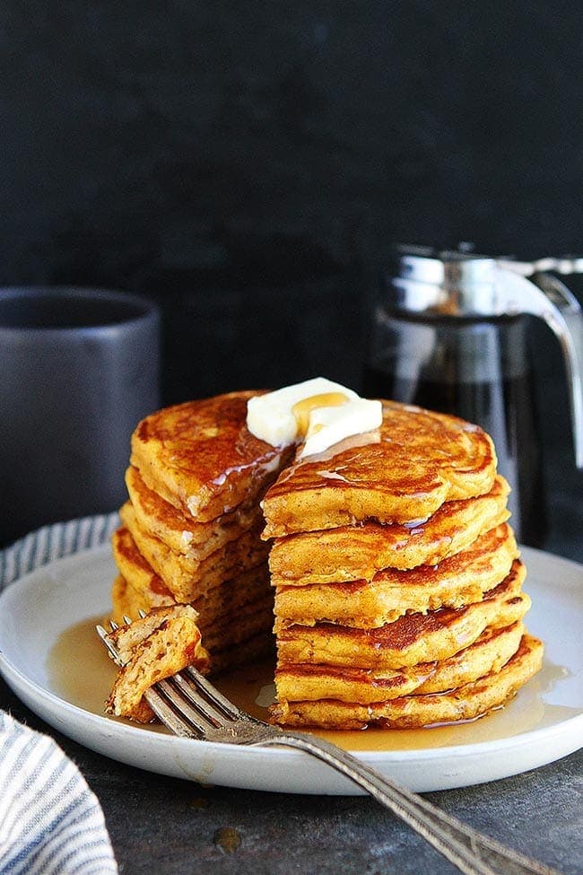 stack of pumpkin pancakes with butter and maple syrup on plate with fork. 