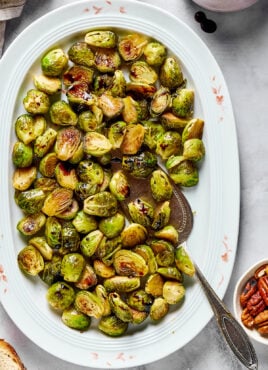 A white oval tray full of roasted brussels sprouts, with a serving spoon in it