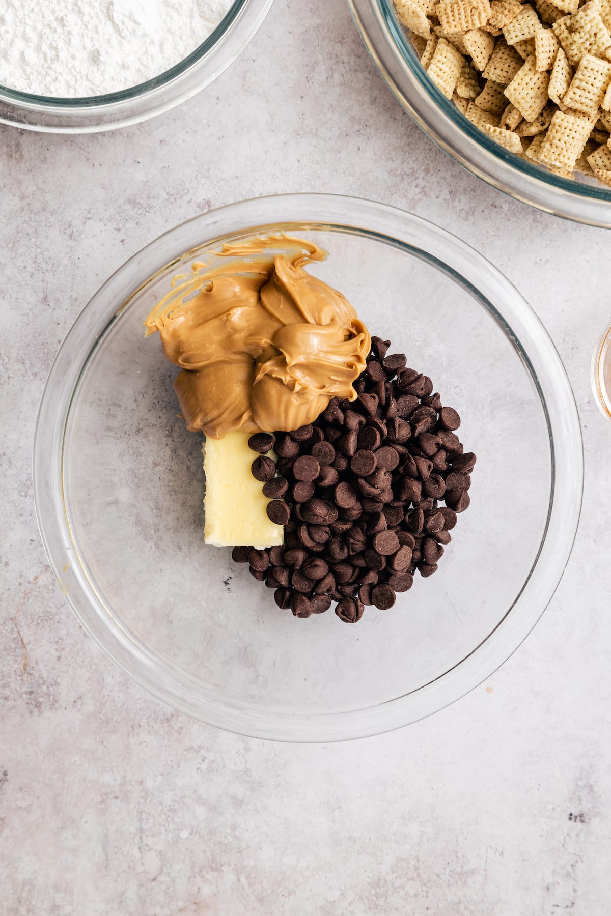 Homemade Puppy Chow is easy to make and SO addicting. This recipe for chocolate peanut butter-covered Chex cereal is a perfect party snack! Peanut butter, chocolate chips, and butter combined in a glass mixing bowl.