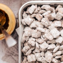 Overhead view of the corner of a metal pan filled with puppy chow next to a jar of peanut butter and a bowl of chocolate chips.