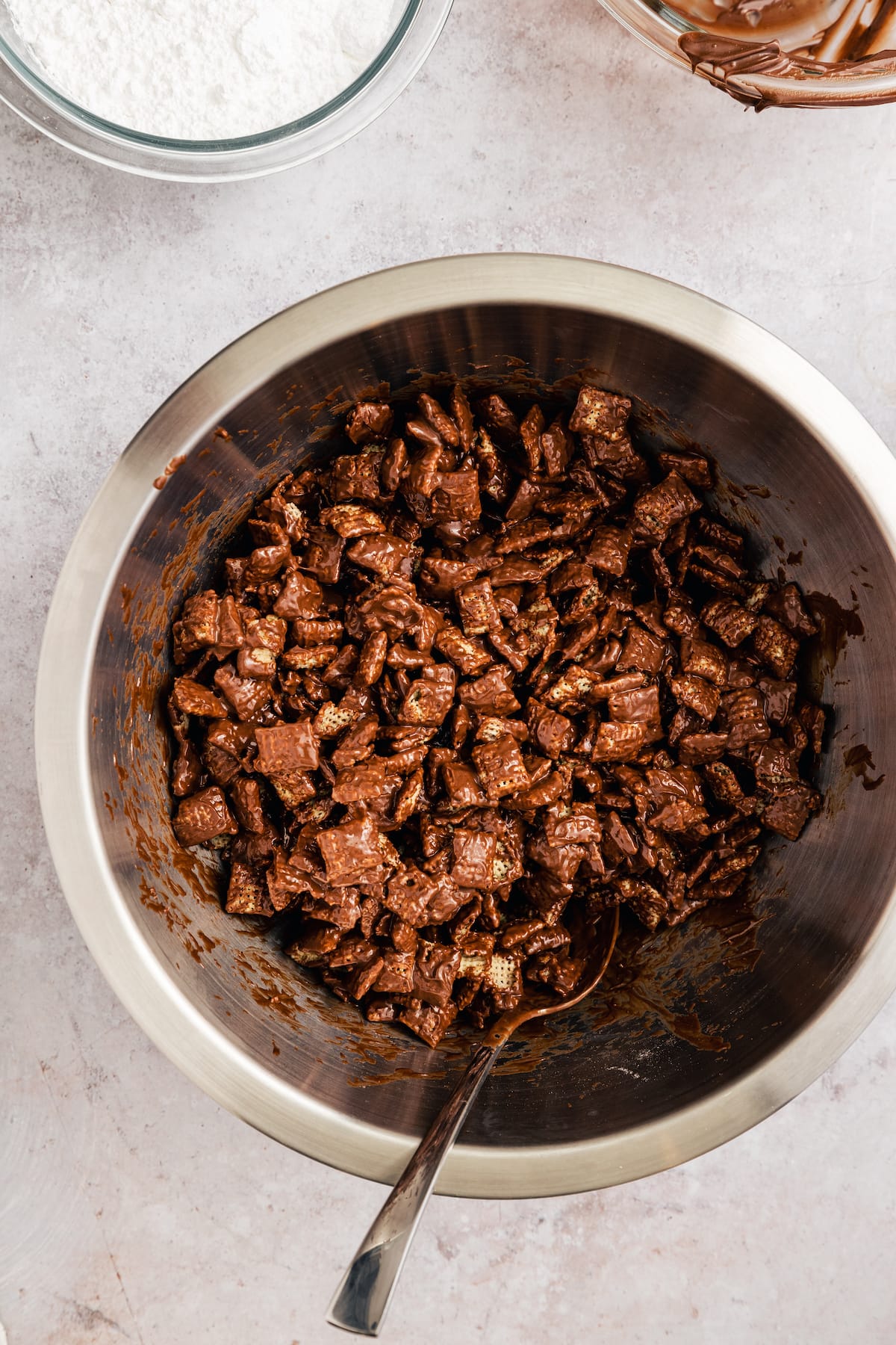 Chex cereal coated in a chocolate peanut butter mixture in a large metal bowl.