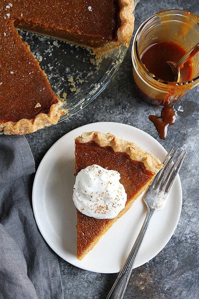 Overheat shot of a piece of Salted Caramel Pumpkin Pie with whipped cream on plate with a fork.