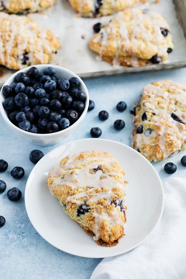 blueberry scone on plate with bowl of blueberries. 