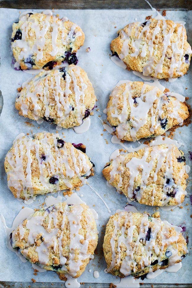 Blueberry scones with glaze on baking sheet with parchment paper. 