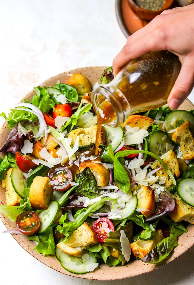 salad dressing being poured on green salad.