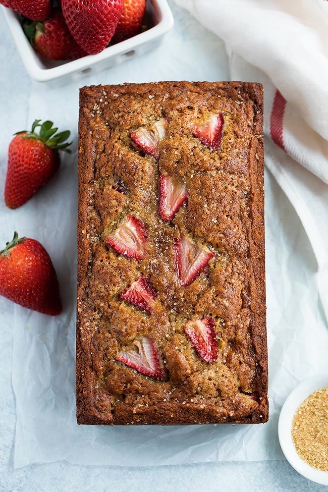 loaf of strawberry banana bread with fresh strawberries.
