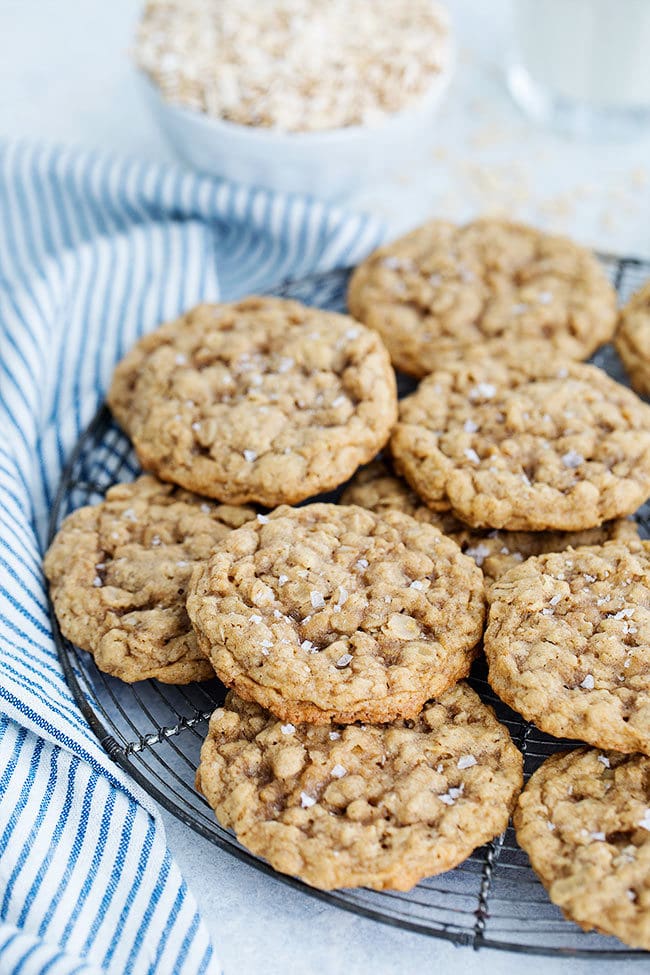 Oatmeal cookies stacked on cooling rack with striped tea towel.