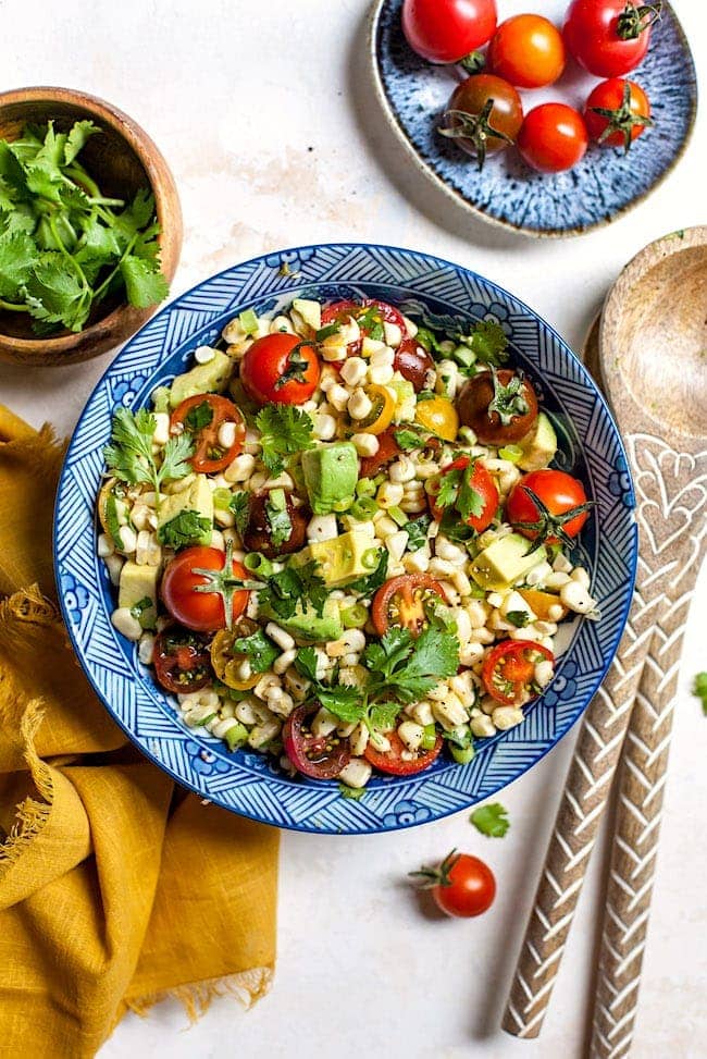 Corn Salad in bowl with tomatoes, avocado, and cilantro. 