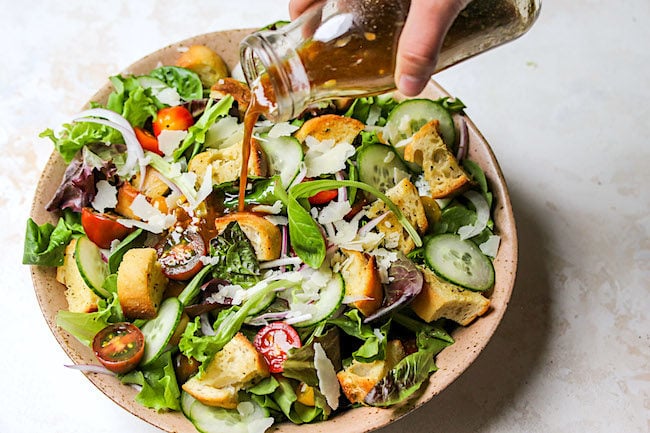 Green Salad in bowl with balsamic vinaigrette being poured over the top. 