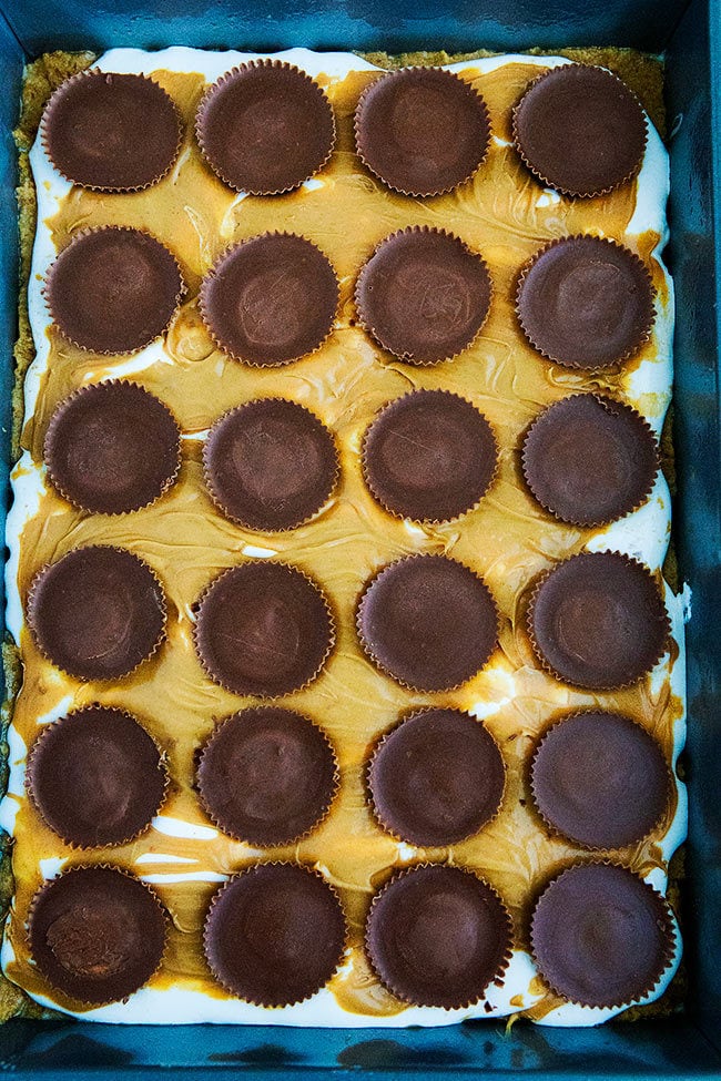 Peanut Butter S'mores Bars being layered in pan with peanut butter cups on top.