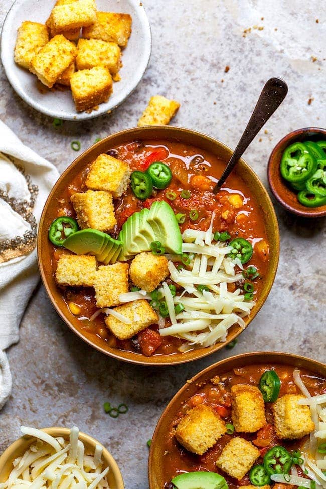 pumpkin chili with cornbread croutons in bowl with toppings and spoon. 