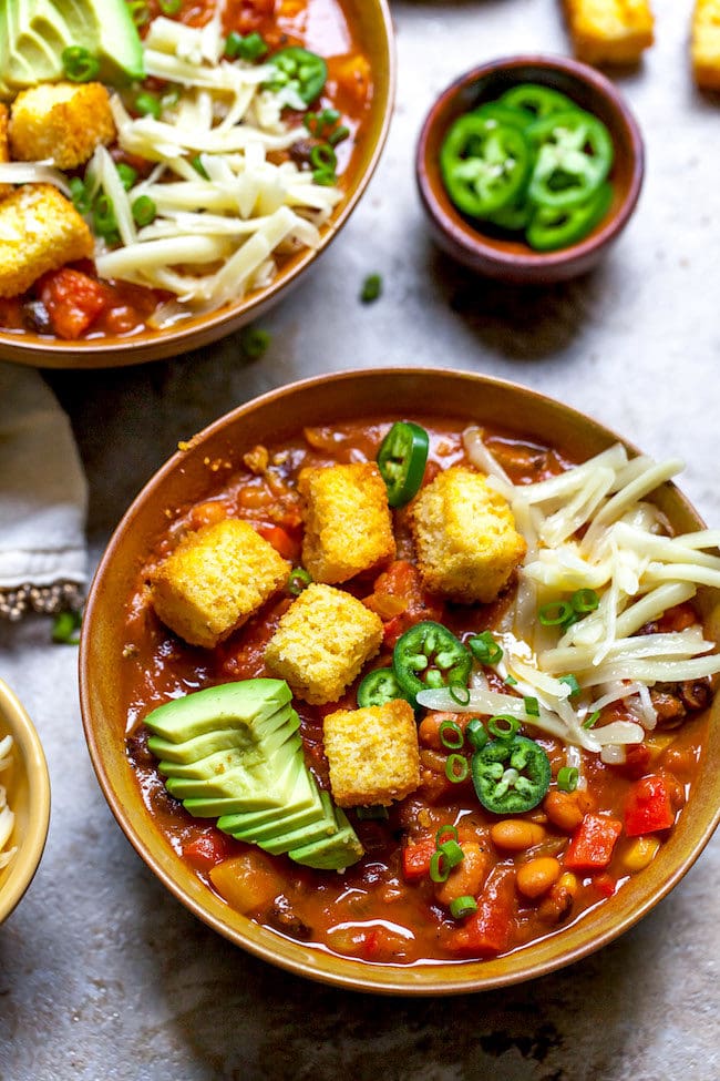 pumpkin chili in bowl with cornbread croutons and toppings. 