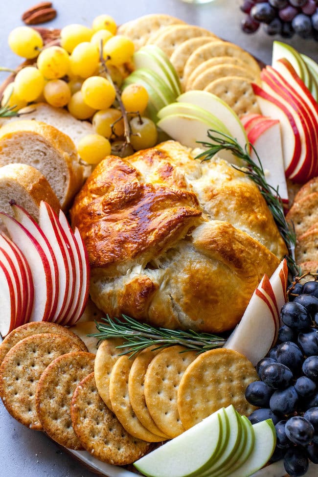 Baked Brie in puff pastry with herbs, apple slices, crackers, and grapes.
