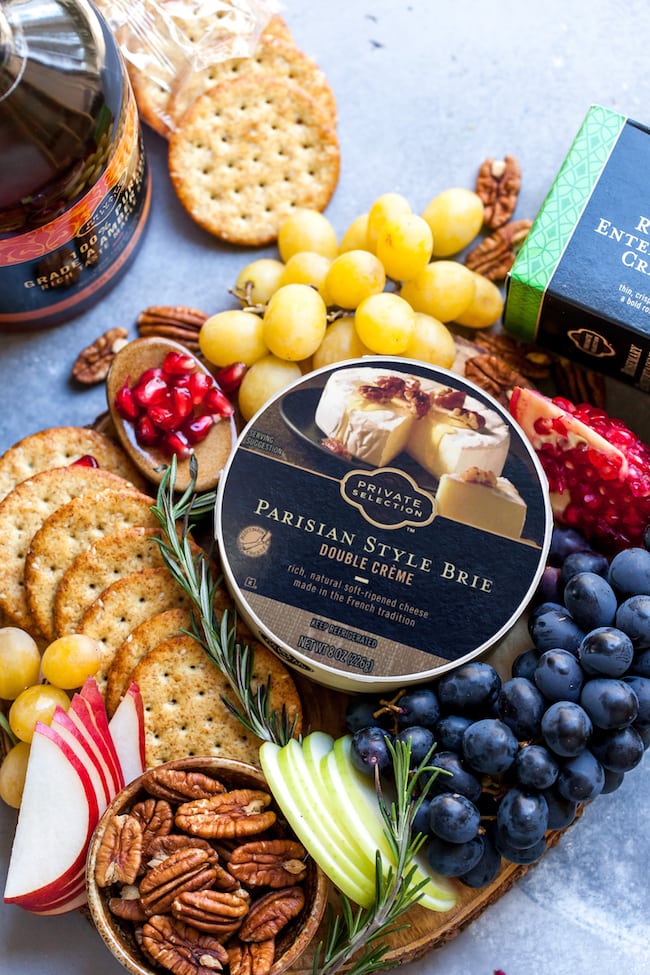 container of brie with fruit, crackers, and pecans.