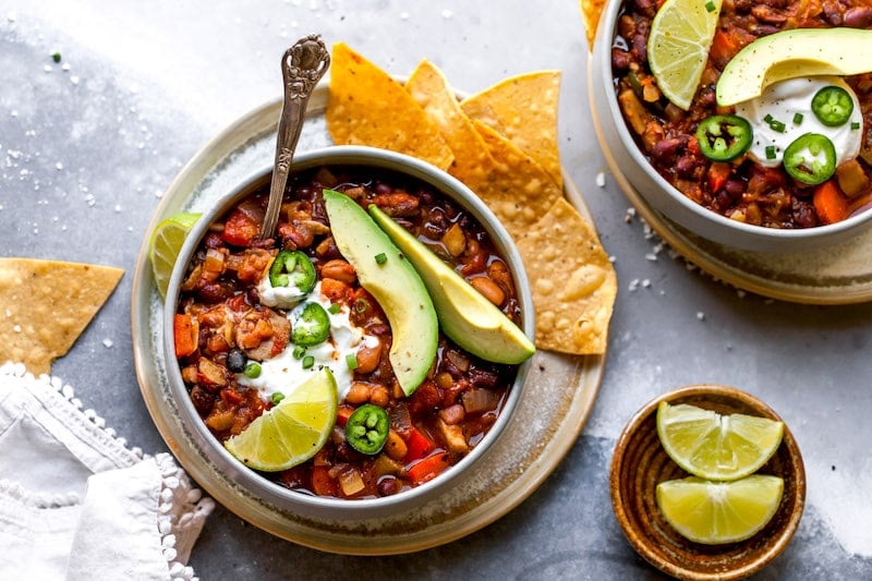 vegetarian chili in bowls with toppings and tortilla chips. 