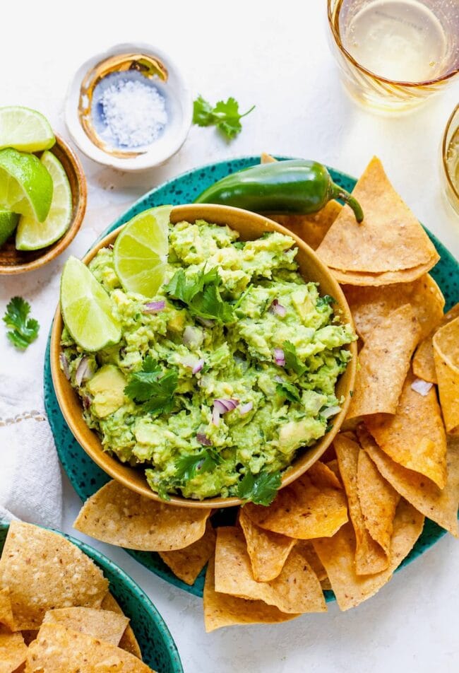 Guacamole in bowl on plate with tortilla chips. 