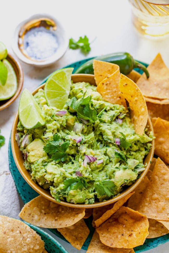 guacamole in bowl with lime wedges and tortilla chips. 