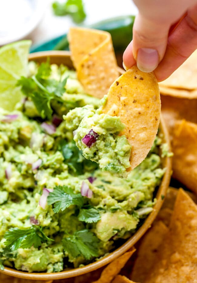 tortilla chip being dipped in a bowl of chunky guacamole.